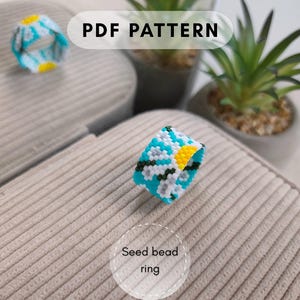 May include: A seed bead ring featuring a daisy pattern with a bright yellow center, white petals, and dark green stems against a vibrant turquoise background. The text PDF PATTERN and Seed bead ring are visible in the image.