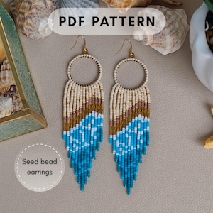 Op de afbeelding: Een paar handgemaakte seed bead oorbellen met een cirkelvormige bovenkant en een gefranjerde onderkant. De oorbellen hebben een kleurengradiënt van witte, gouden en blauwe kralen. De tekst "PDF PATTERN" staat bovenaan en "Seed bead earrings" onderaan.