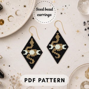 May include: Diamond-shaped seed bead earrings featuring a black background with a gold snake and a central white moon phase motif. The earrings hang from gold-toned metal hooks. The text Seed bead earrings and PDF PATTERN is visible.