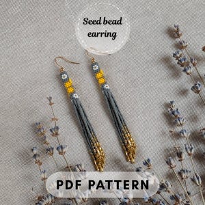 May include: A pair of long, dangling seed bead earrings featuring a pattern of grey, yellow, and white beads with gold-toned accents at the bottom. The text "Seed bead earring" and "PDF PATTERN" is visible on the image, indicating a design guide.