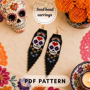 May include: A pair of long, black seed bead earrings featuring a white skull design with a red heart on the forehead and colorful floral accents. The earrings are displayed alongside a decorative skull and orange flowers with text reading Seed bead earrings and PDF PATTERN.
