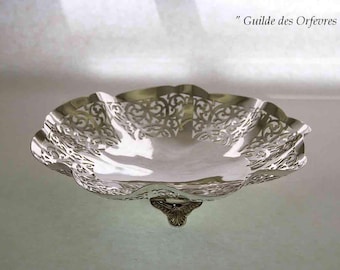 May include: A silver-colored decorative bowl with a scalloped edge and intricate openwork design. The bowl has a small, ornate foot and the text "Guilde des Orfevres" is visible.