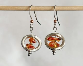 May include: Silver dangle earrings with a circular design and amber stones inside. The earrings have a small silver ball at the bottom.