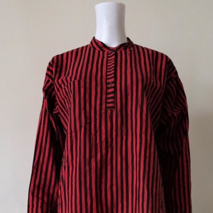 Op de afbeelding: Een rood-wit gestreept overhemd met lange mouwen, een mandarijnkraag en een enkele knoopsluiting. Het overhemd heeft een losse pasvorm en is gemaakt van een lichtgewicht stof.