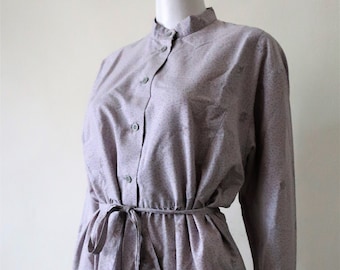 May include: A long-sleeved, gray dress with a small floral print. The dress has a mandarin collar, a button-up front, and a tie at the waist.
