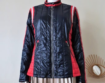 May include: A black quilted jacket with red and white stripes on the sleeves. The jacket has a zipper closure and a stand-up collar.