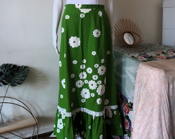 May include: A long green skirt with a white floral pattern and a lace trim. The skirt is on a mannequin.