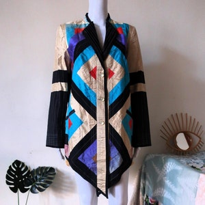 Puede incluir: Una chaqueta larga y asimétrica con un patrón geométrico en tonos de azul, negro, beige y morado. La chaqueta tiene cierre de botón y cuello.