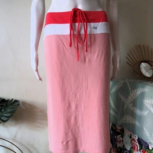 Puede incluir: Una falda rosa con una cintura blanca y roja y un cordón. La cintura tiene la palabra "LACOSTE" impresa.