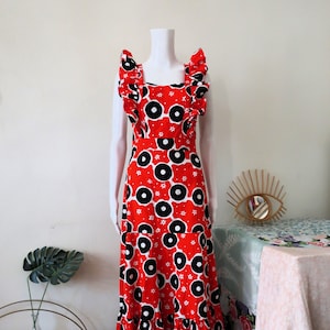 May include: A red maxi dress with a black and white geometric print. The dress has a square neckline and ruffled straps. The dress is made of a lightweight fabric and has a flowy silhouette.