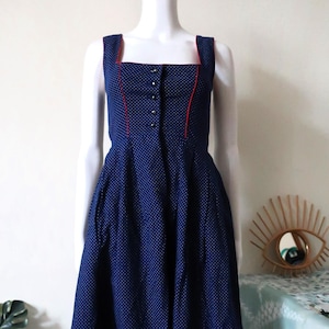 May include: A navy blue dress with white polka dots and red trim. The dress has a square neckline and a button-up front.