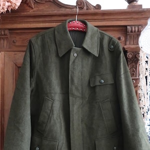 May include: A dark green wool jacket with a button closure, two flap pockets, and two buttoned pockets on the chest. The jacket has a collar and is hanging on a red studded hanger.