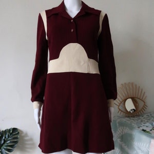 Puede incluir: Un vestido mini color burdeos con mangas largas y un diseño geométrico blanco. El vestido tiene cuello y cierre de botón.