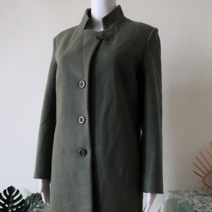 May include: A long, olive green coat with a mandarin collar and four buttons down the front. The coat has a decorative clasp at the collar.