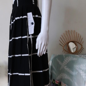 Pode incluir: Uma saia xadrez preta e branca com um bolso de remendo branco e um fecho de botão. A saia é de comprimento até ao joelho e tem um design plissado.