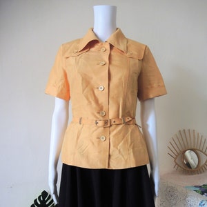 May include: A yellow short-sleeved collared shirt with a belt and a black skirt.