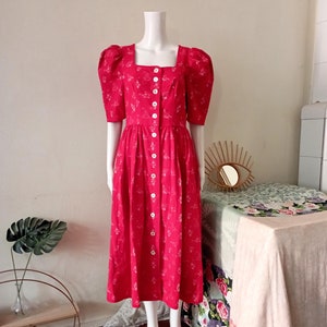 May include: A red midi dress with a white floral print and a button-up front. The dress has puffed sleeves and a square neckline.