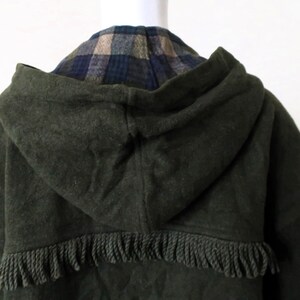 May include: Dark green hooded coat with a fringed hem. The hood reveals a plaid pattern in shades of blue, tan, and green. The coat is made of a thick, textured fabric.