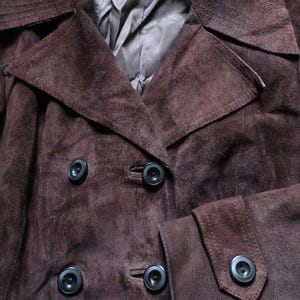 May include: A brown suede jacket with a double breasted closure and a large collar. The jacket has four black buttons.