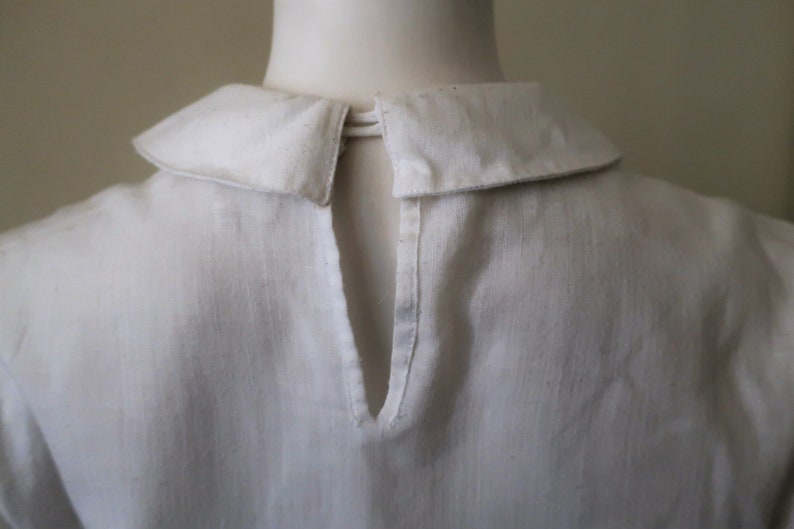 May include: White collared shirt with a keyhole opening in the back.