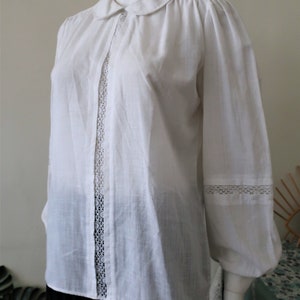 May include: White long-sleeved blouse with a peter pan collar and lace trim on the front and cuffs.