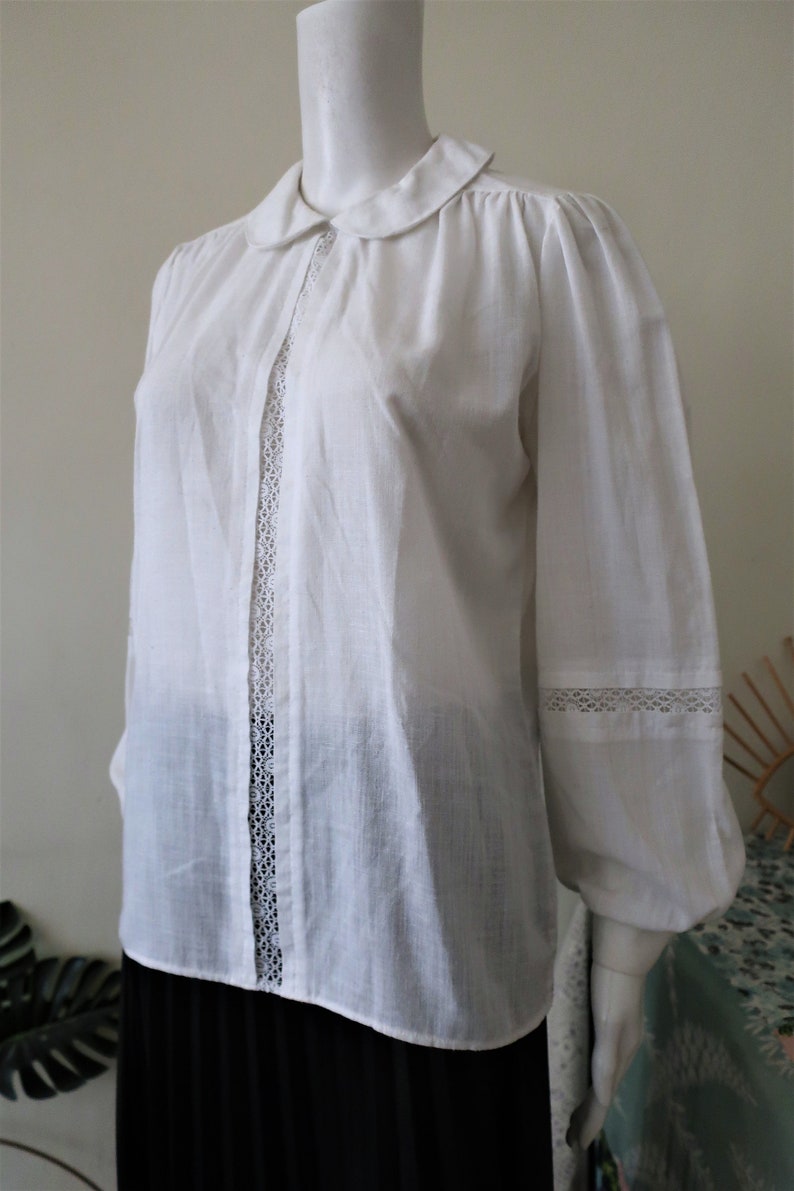 May include: White long-sleeved blouse with a peter pan collar and lace trim on the front and cuffs.