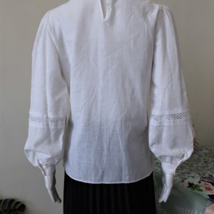 May include: White long-sleeved blouse with a Peter Pan collar and lace trim on the cuffs. The blouse is made of a lightweight fabric and has a relaxed fit.