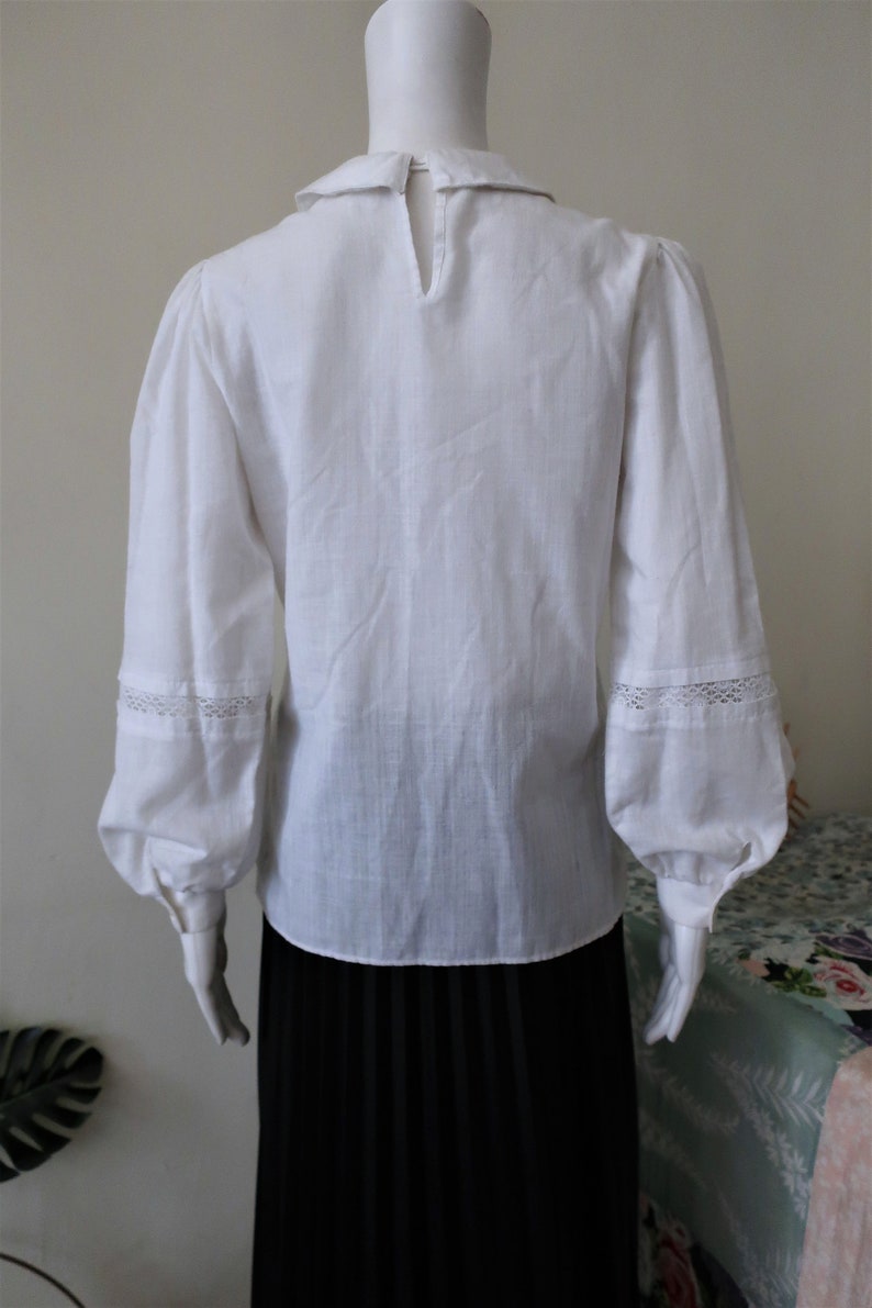 May include: White long-sleeved blouse with a Peter Pan collar and lace trim on the cuffs. The blouse is made of a lightweight fabric and has a relaxed fit.