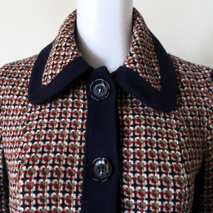 May include: A navy blue and red patterned jacket with a collar and button closure. The jacket has a geometric pattern and a dark blue trim.