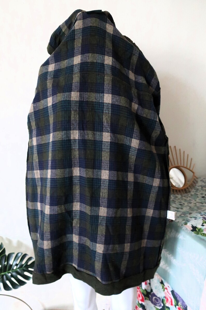 May include: A dark green, navy blue, and tan plaid jacket. The jacket has a hood and a dark green trim at the bottom. The plaid pattern is a classic design, suitable for fall or winter wear. The jacket is made of a soft, woven fabric.