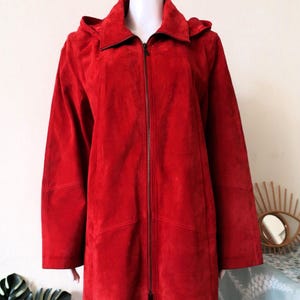 Può includere: Una lunga giacca di camoscio rosso con cappuccio e chiusura a zip.