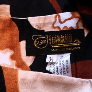 May include: A black and brown patterned dress with a gold label that reads "Heikkil&auml; Oy" and "Made in Finland". The label also includes a size tag that says "34".
