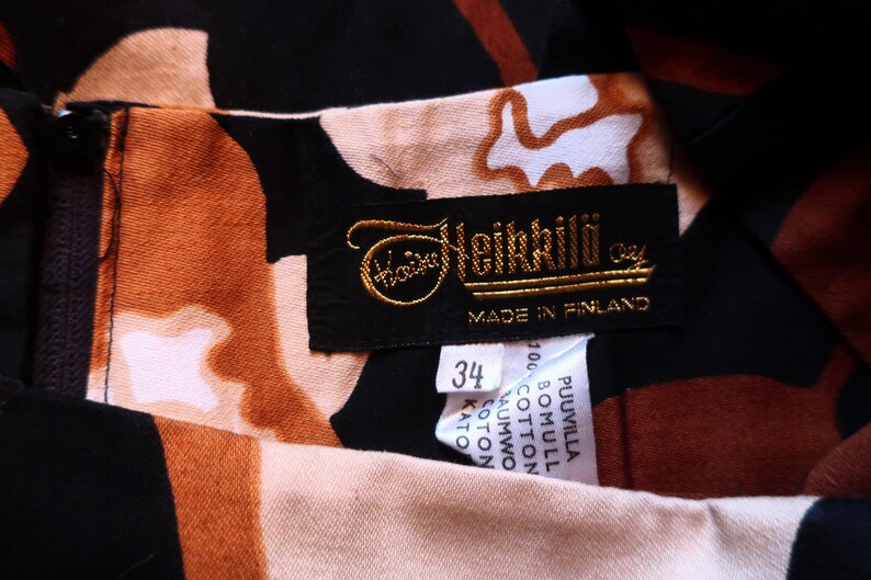 May include: A black and brown patterned dress with a gold label that reads "Heikkil&auml; Oy" and "Made in Finland". The label also includes a size tag that says "34".