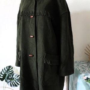 May include: Dark green hooded coat with fringe detailing and wooden toggle closures. The coat features two front pockets with fringe and a plaid lining in the hood. A vintage style coat.