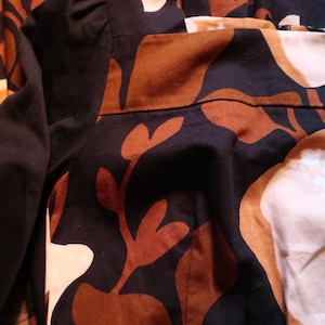 May include: A black and brown patterned dress with a long sleeve. The dress has a floral pattern with brown and white leaves.