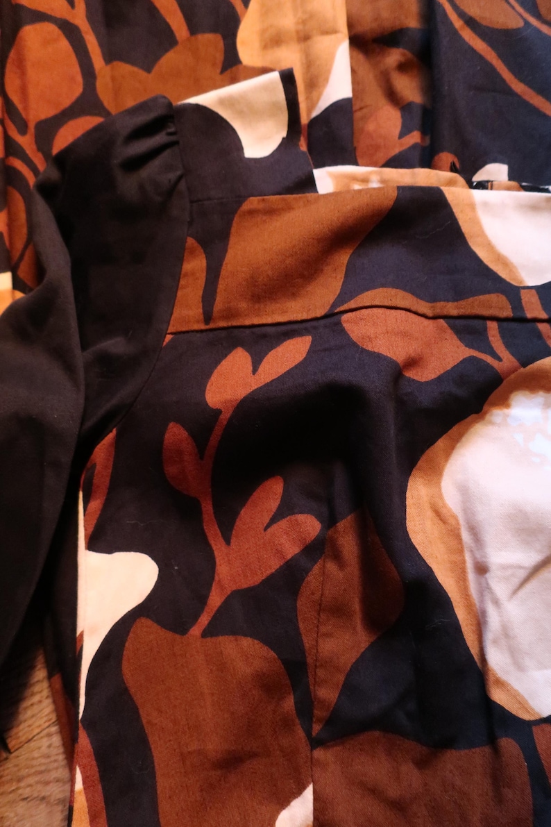 May include: A black and brown patterned dress with a long sleeve. The dress has a floral pattern with brown and white leaves.
