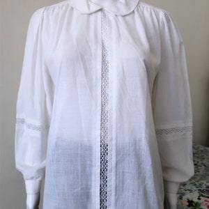 May include: A white cotton blouse with a peter pan collar and lace trim down the front and on the sleeves.