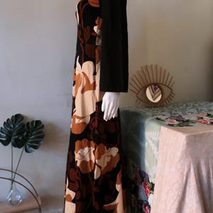 May include: A long, black velvet dress with a floral print in shades of brown and cream. The dress has long sleeves and a scoop neck.