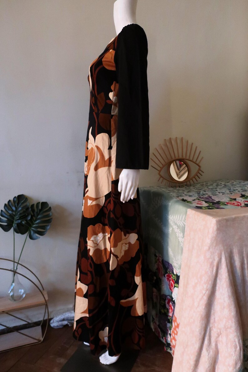 May include: A long, black velvet dress with a floral print in shades of brown and cream. The dress has long sleeves and a scoop neck.
