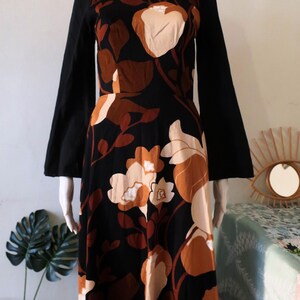 May include: A long-sleeved maxi dress with a black background and a floral print in shades of brown and cream. The dress has a square neckline and bell sleeves.