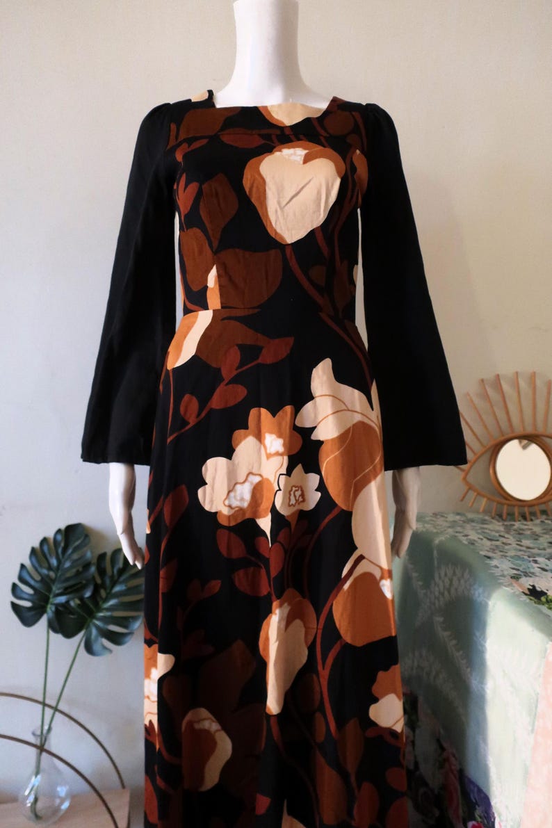May include: A long-sleeved maxi dress with a black background and a floral print in shades of brown and cream. The dress has a square neckline and bell sleeves.