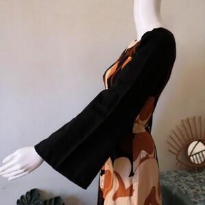 May include: A long-sleeved dress with a brown, black, and white abstract print. The dress has a wide, bell-shaped sleeve.