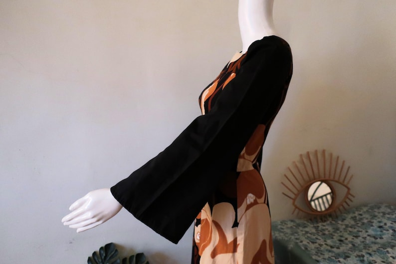 May include: A long-sleeved dress with a brown, black, and white abstract print. The dress has a wide, bell-shaped sleeve.
