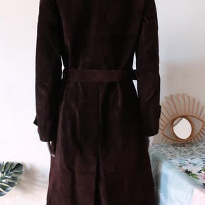 May include: A brown suede trench coat with a belt. The coat has a classic design and is perfect for fall or winter.