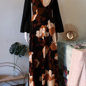 May include: A long black maxi dress with a floral print in shades of brown and cream. The dress has a square neckline and long bell sleeves.