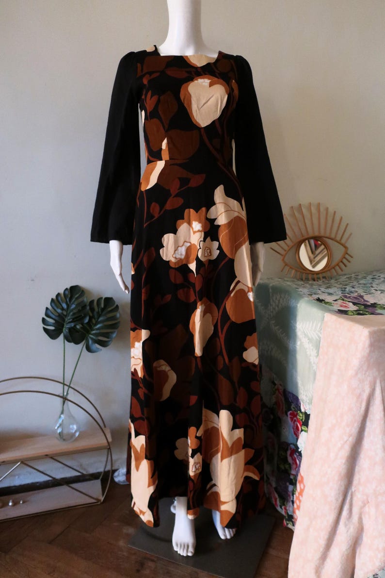 May include: A long black maxi dress with a floral print in shades of brown and cream. The dress has a square neckline and long bell sleeves.