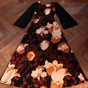 May include: A long, black and brown floral print dress with long bell sleeves. The dress has a square neckline and a fitted bodice.