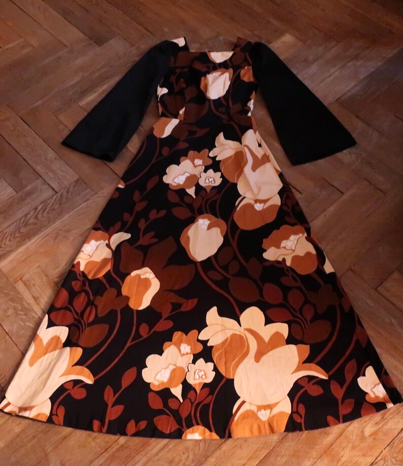 May include: A long, black and brown floral print dress with long bell sleeves. The dress has a square neckline and a fitted bodice.