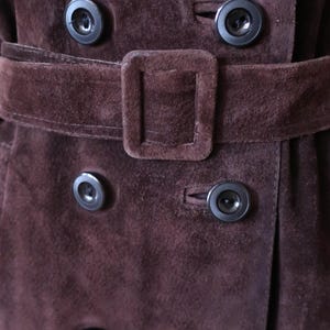 May include: Close-up of a brown suede jacket with a belt and multiple black buttons.