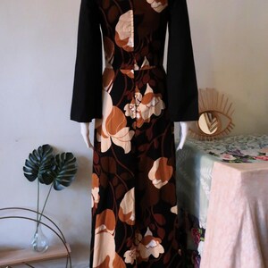 May include: A long black and brown floral maxi dress with long bell sleeves. The dress has a square neckline and a fitted bodice.